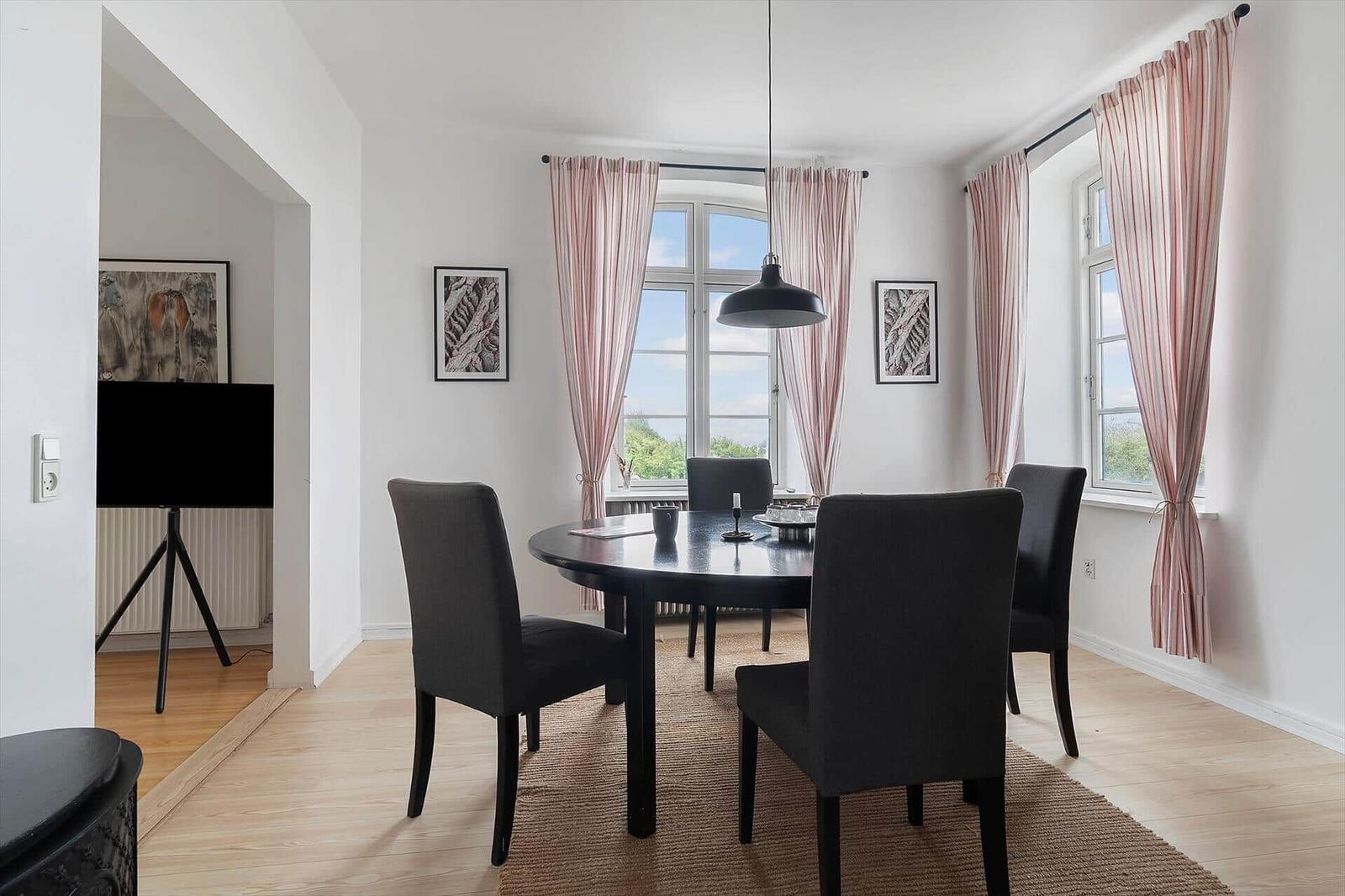 Esszimmer mit runder Tisch, vier Stühlen und Fenstern mit rosa Vorhängen.