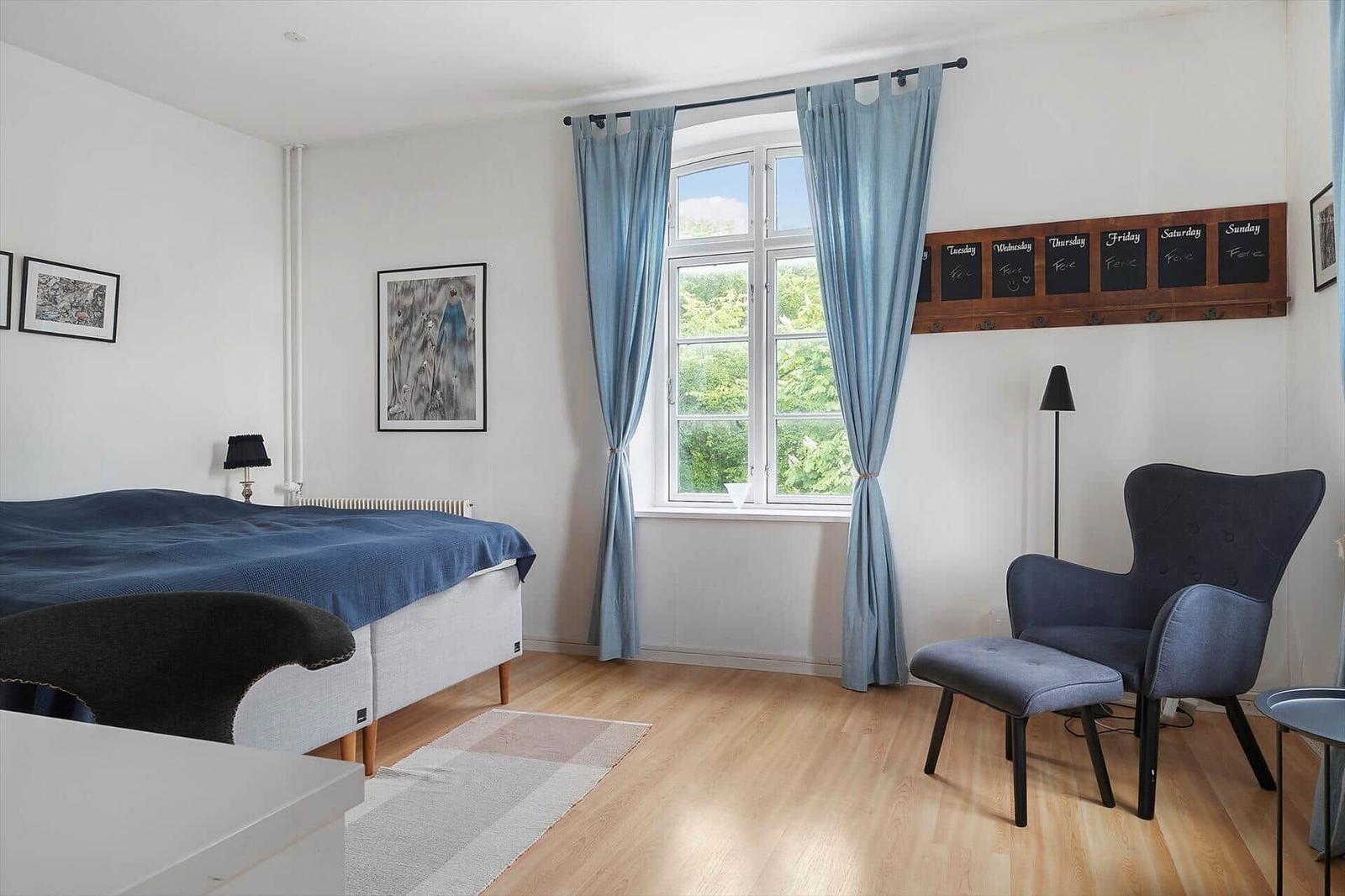 Schlafzimmer mit Bett, Stuhl und Fenster mit Blick auf Grün