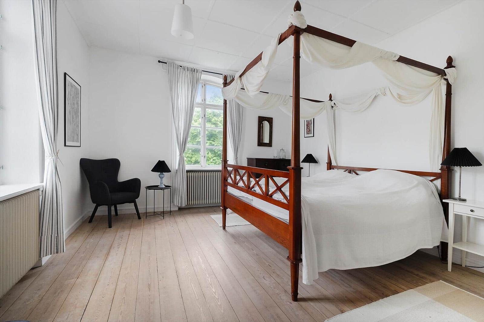 Schlafzimmer mit Holzboden, Bett mit Baldachin und Sessel.