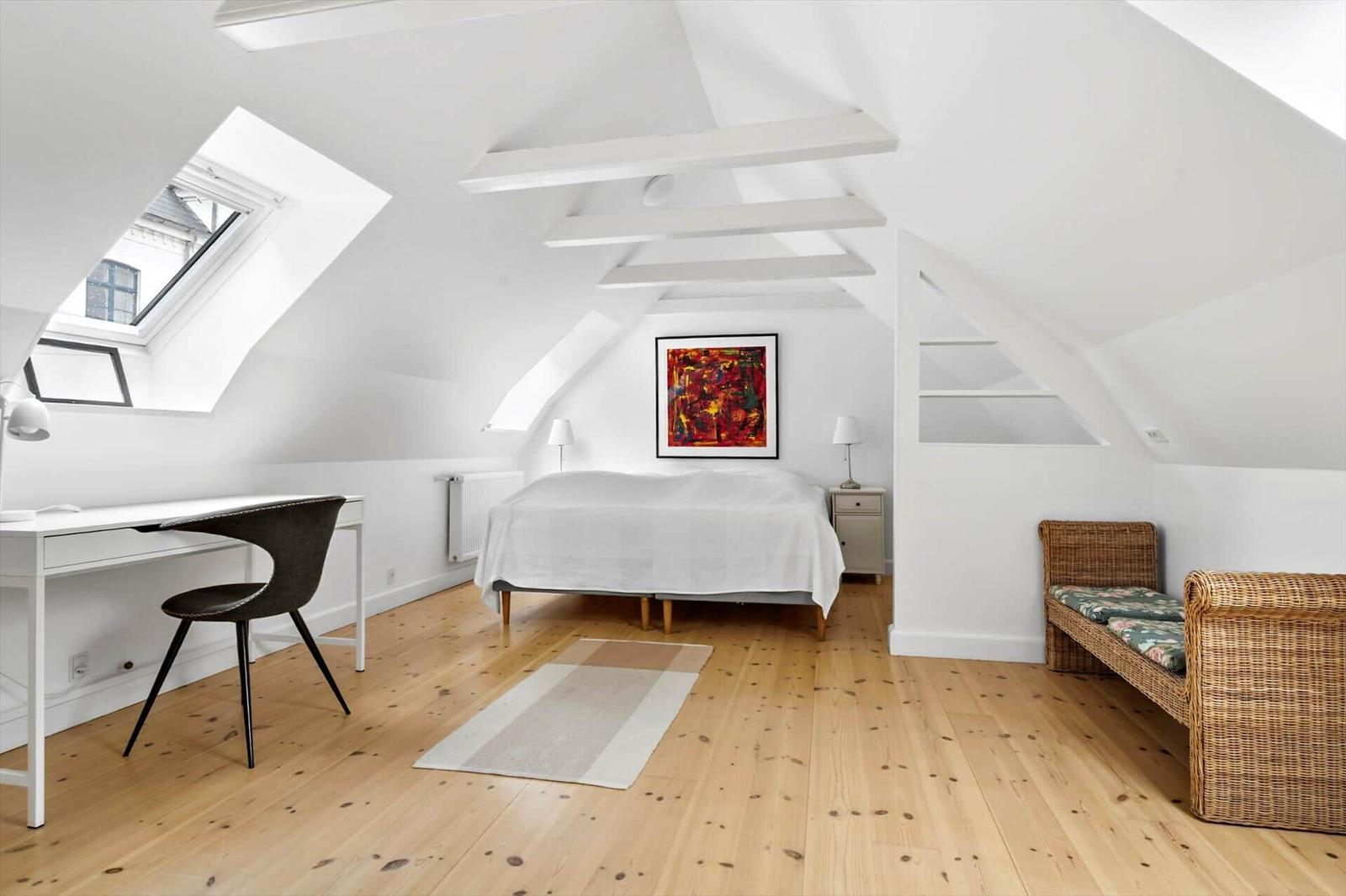 Schlafzimmer mit Dachschrägen, Schreibtisch, Bett und Rattanbank.
