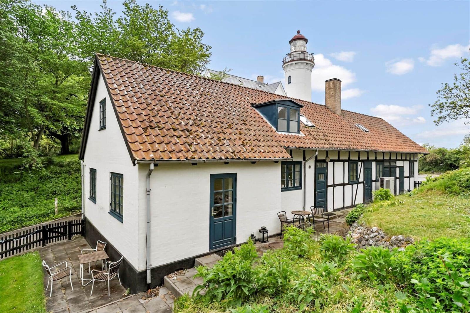Wohnhaus mit rotem Dach und grünen Fensterrahmen, im Hintergrund Leuchtturm.