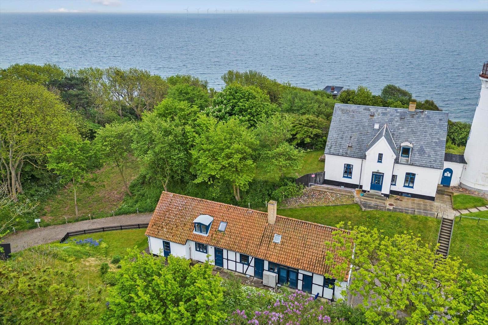 Zwei Häuser mit rotem und grauem Dach, umgeben von Grün und Meer.