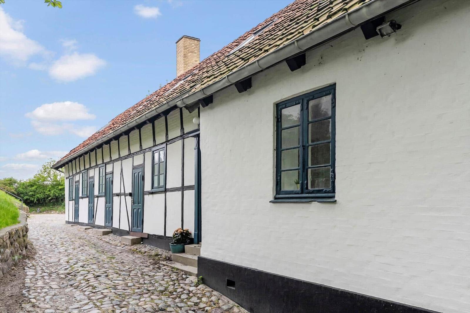 Ferienhaus mit weiß verputzter Fassade, dunklen Fenstern und Steinweg.
