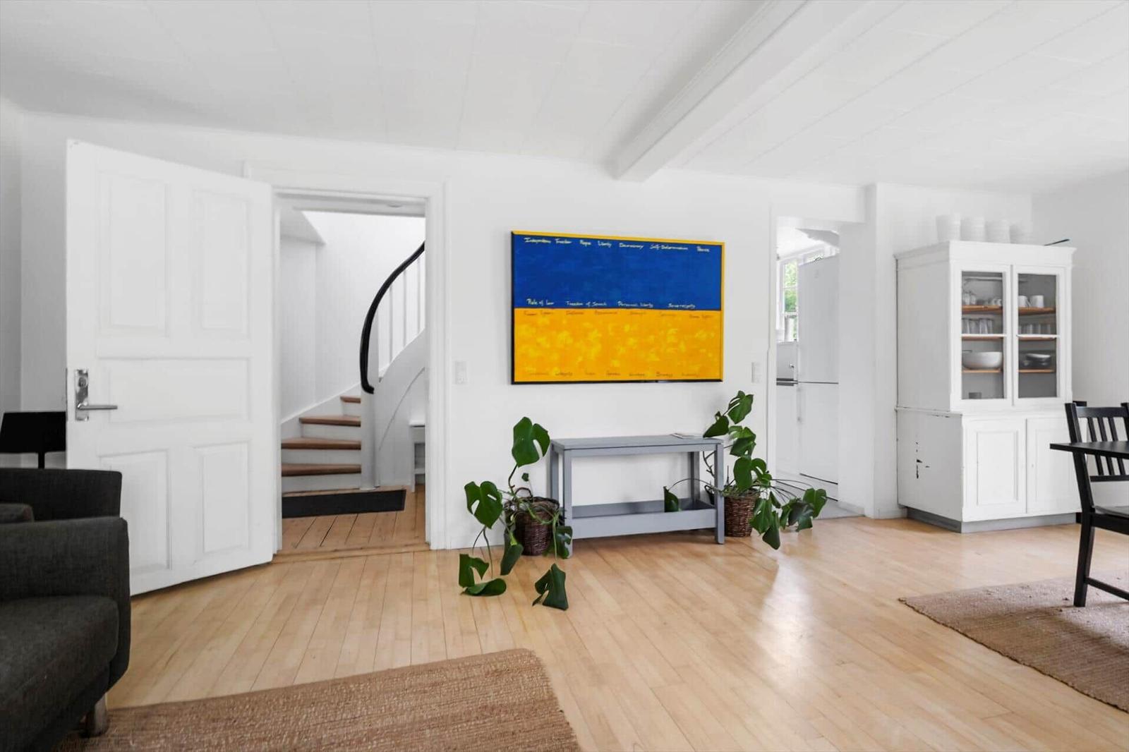 Wohnraum mit Holzboden, weißer Tür, Treppe und Wandbild