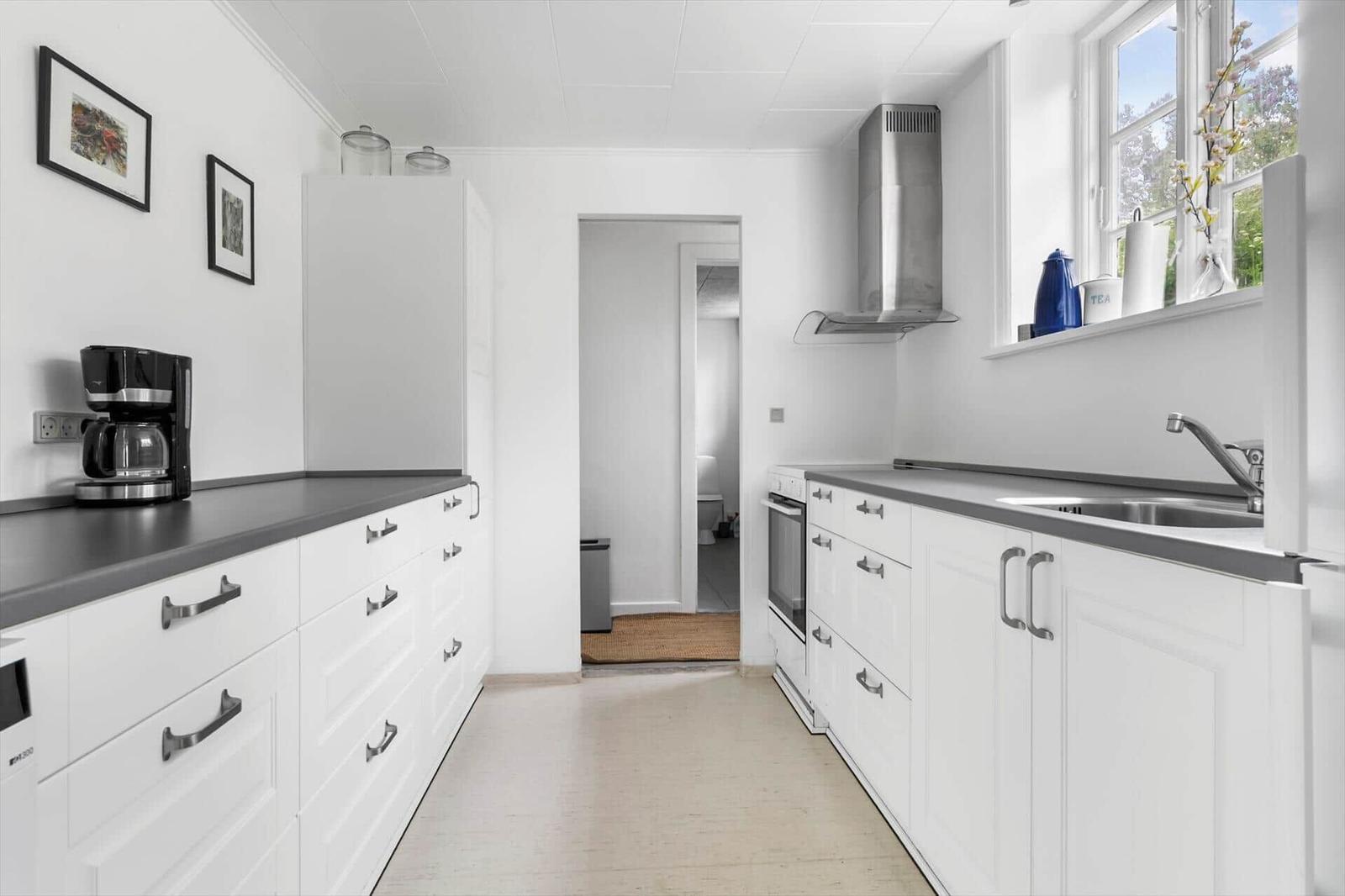 Küche mit weißen Schränken, grauer Arbeitsplatte und Fenster mit Blick nach draußen.
