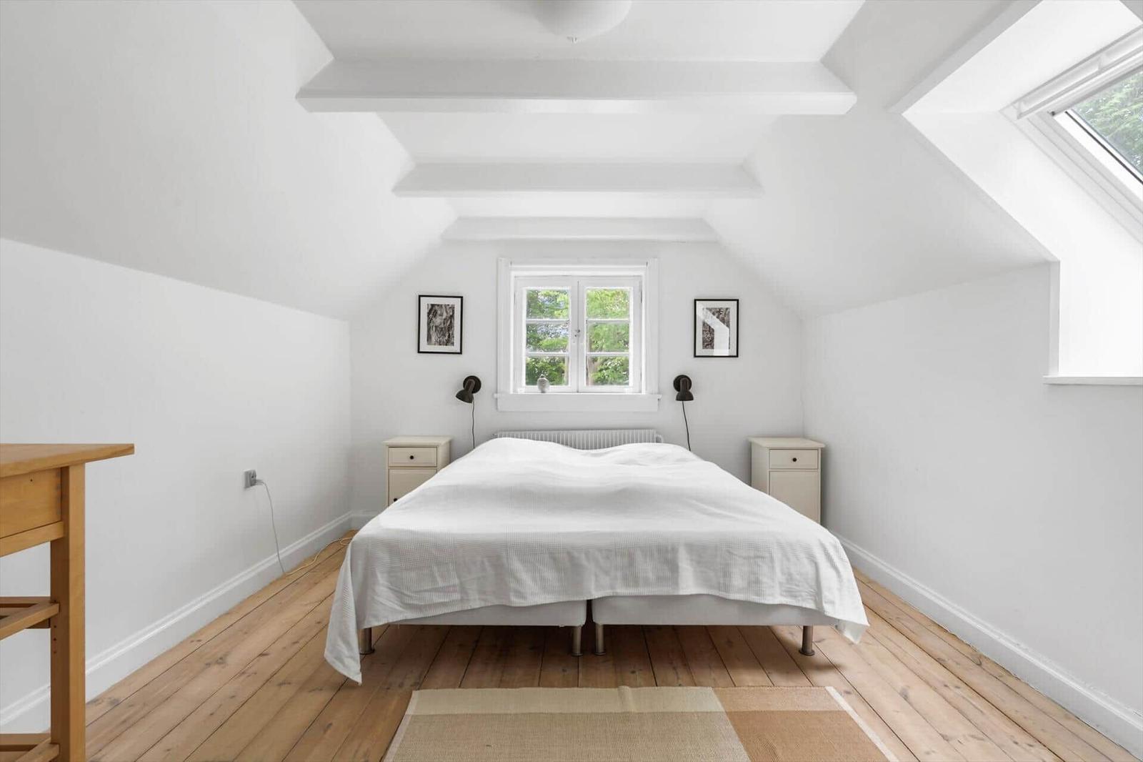Schlafzimmer mit Dachbodenfenster, Holzboden und weißem Bett.