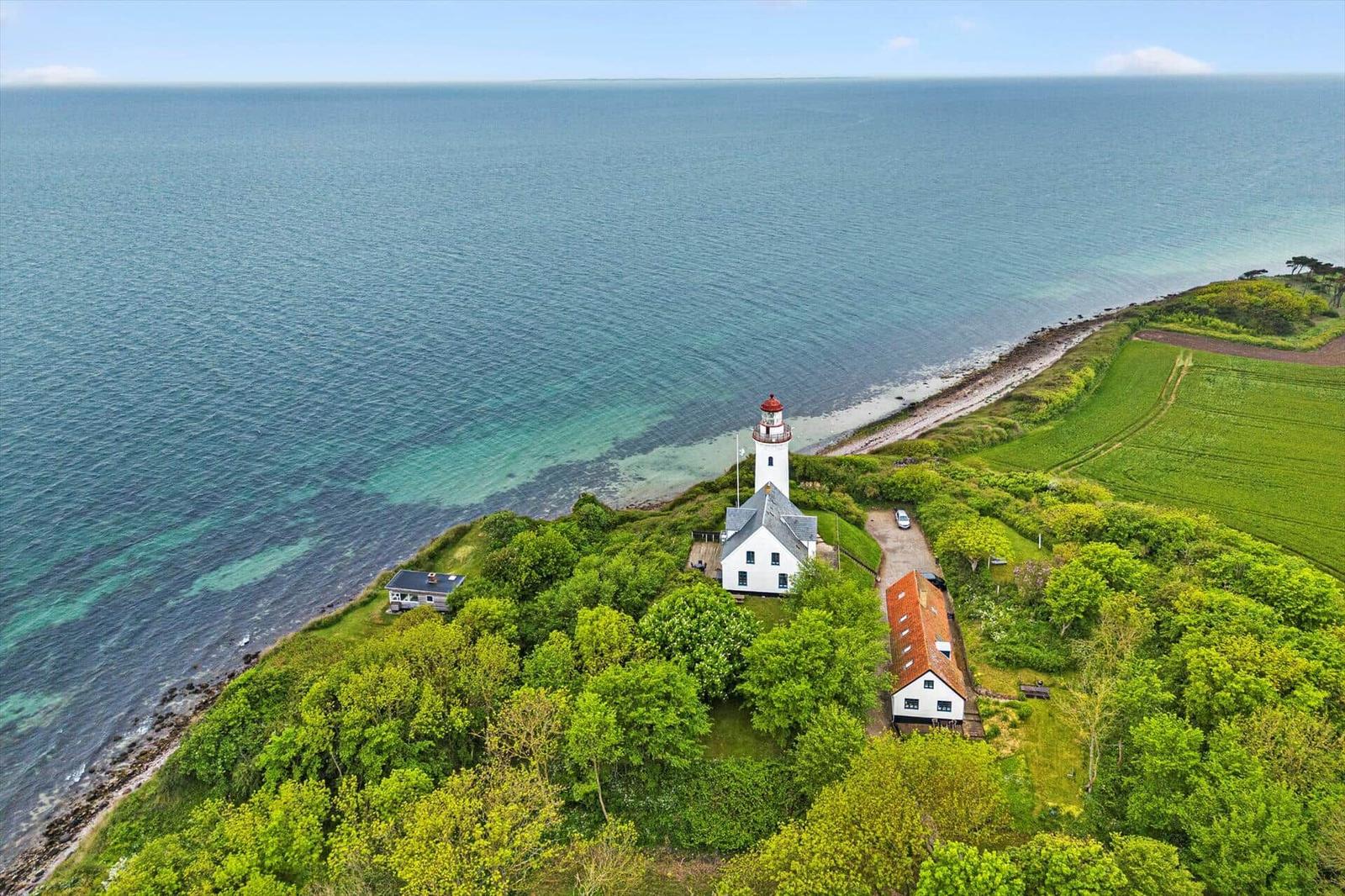 Lichtturm auf Küstenrücken mit grünen Wiesen und Meer im Hintergrund.