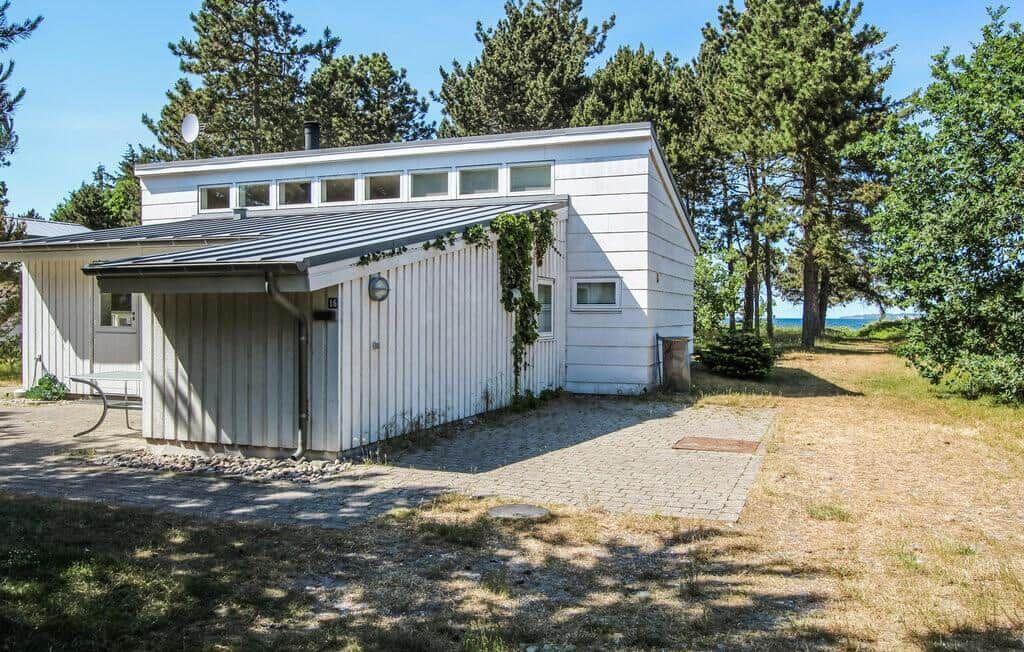 Moderne weiße Hütte mit Balkon, umgeben von Bäumen und Blick aufs Wasser.