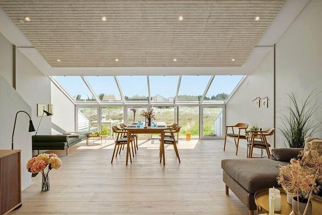 Ein Raum mit Holzboden, Tisch, Stühlen und großem Fensterbereich. Decke mit Holzstruktur.