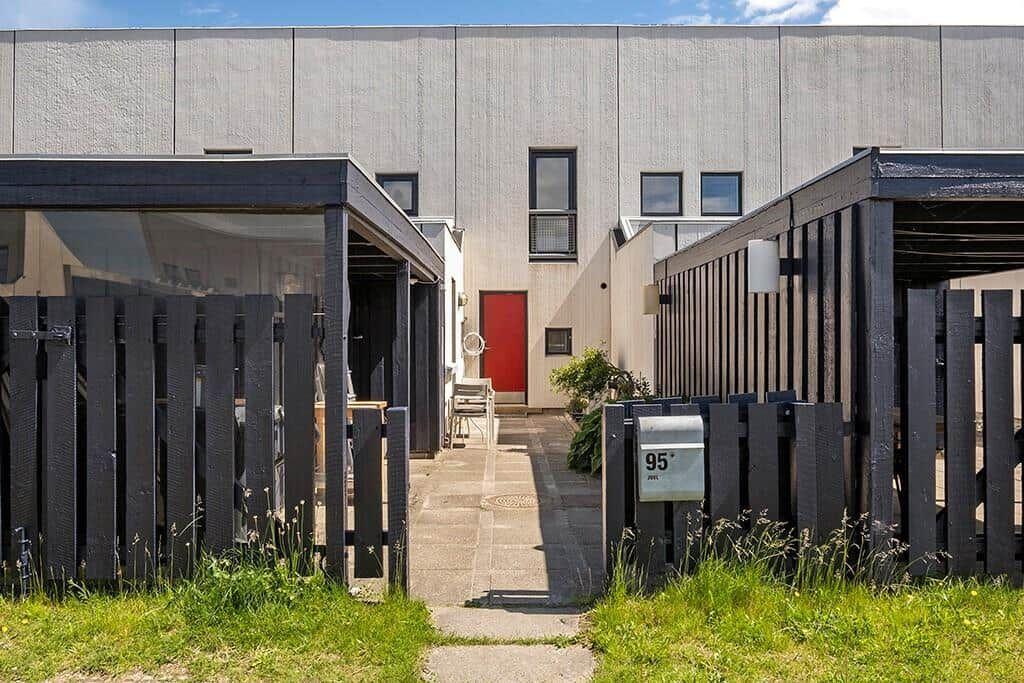 Haus mit roter Tür, gepflastertem Weg und schwarzen Holzgeländern.