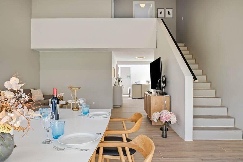 Essbereich mit Tisch und Stühlen, Treppenaufgang und Fernseher im Hintergrund.