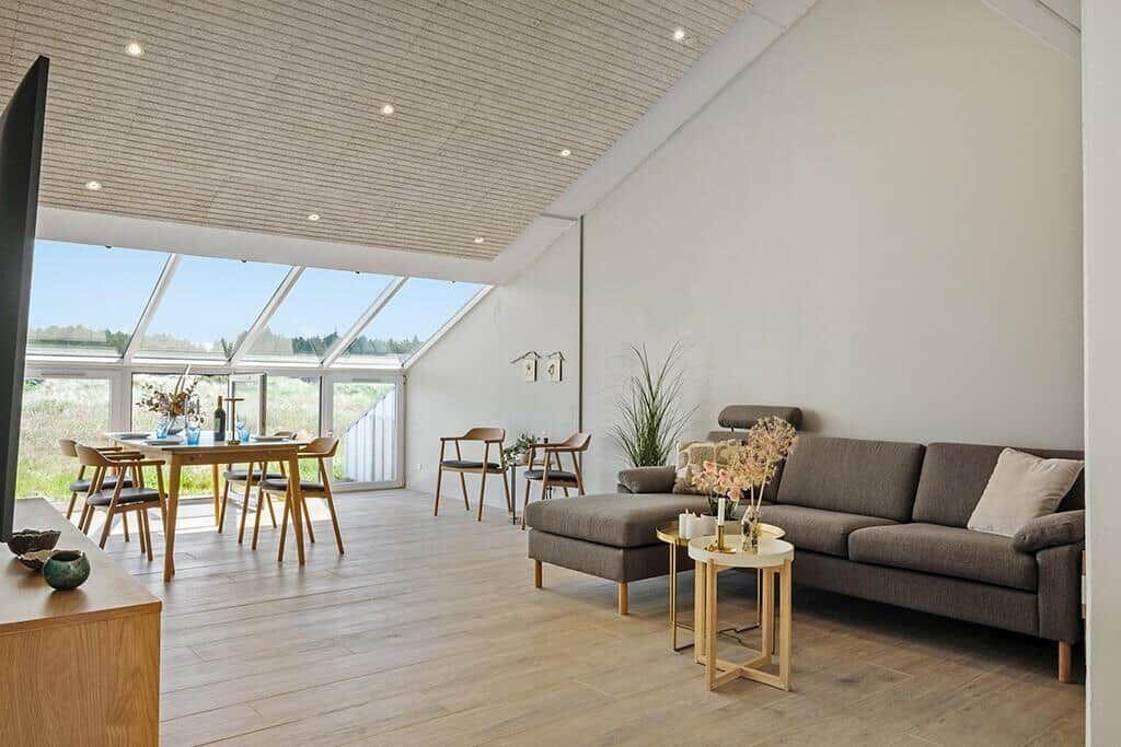 Wohn- und Essbereich mit Sofa, Tisch und Stühlen. Große Fensterfront mit Blick auf Grünland.