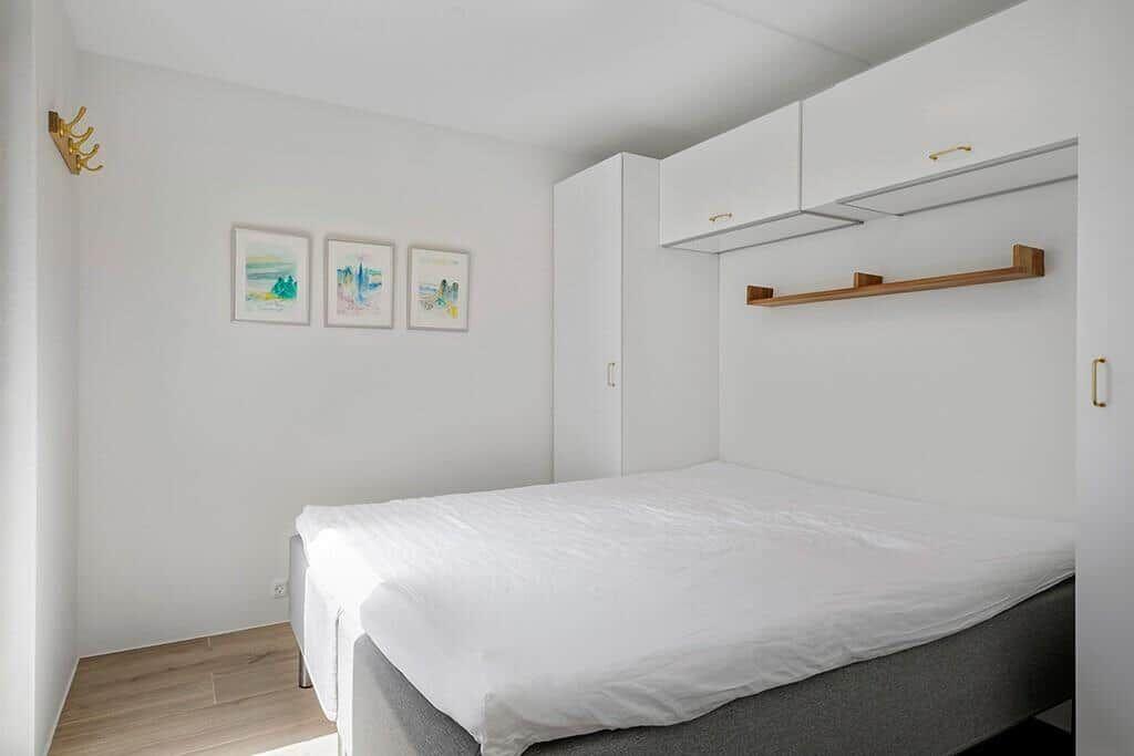 Schlafzimmer mit weißem Bett, weißen Schränken und drei Bildern an der Wand.