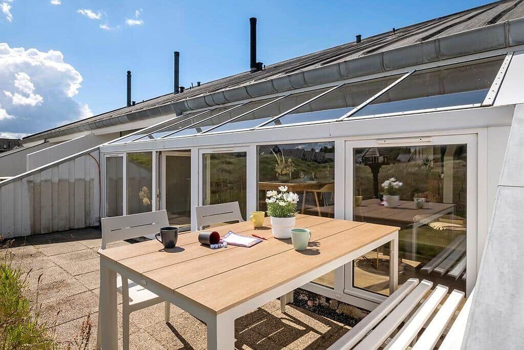 Terrasse mit Tisch und Stühlen vor einer Glasveranda mit Blick auf den Garten.
