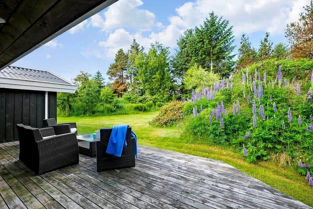 Terrasse mit Sitzgelegenheiten und Blick auf grünen Garten mit Lupinen.