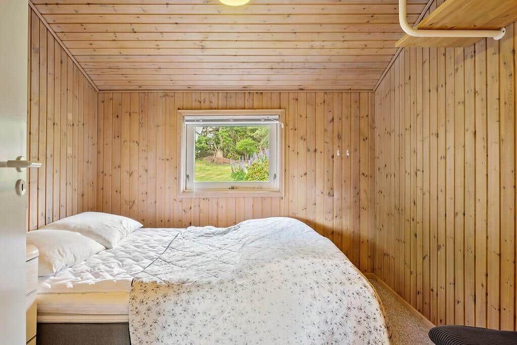 Schlafzimmer mit Holzwandverkleidung und Fenster zur grünen Außenseite.