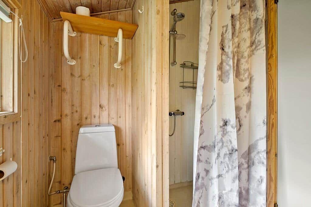 Badezimmer mit Dusche, Toilette und Holzwandverkleidung.