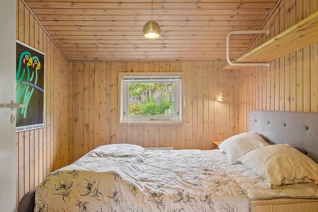 Schlafzimmer mit Holzwand, Bett, Fenster und Wandbild.