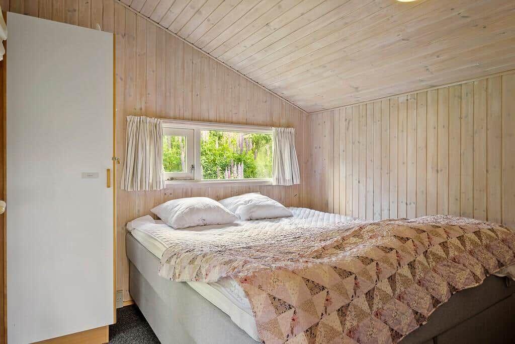 Schlafzimmer mit Bett, Holzwand und Fenster mit Blick auf Grün.