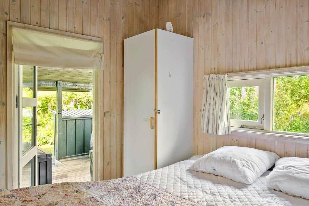 Schlafzimmer mit Bett, Kleiderschrank und Blick auf Balkon und Grün.