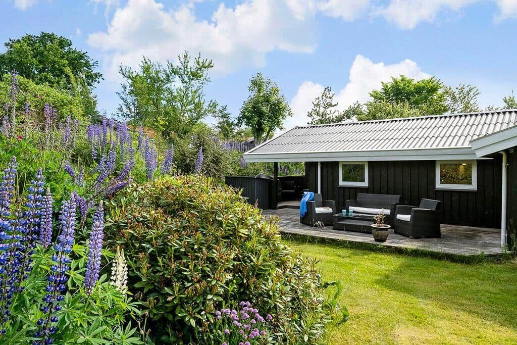 Haus mit Terrasse, Garten und blühenden Lupinen unter blauem Himmel.