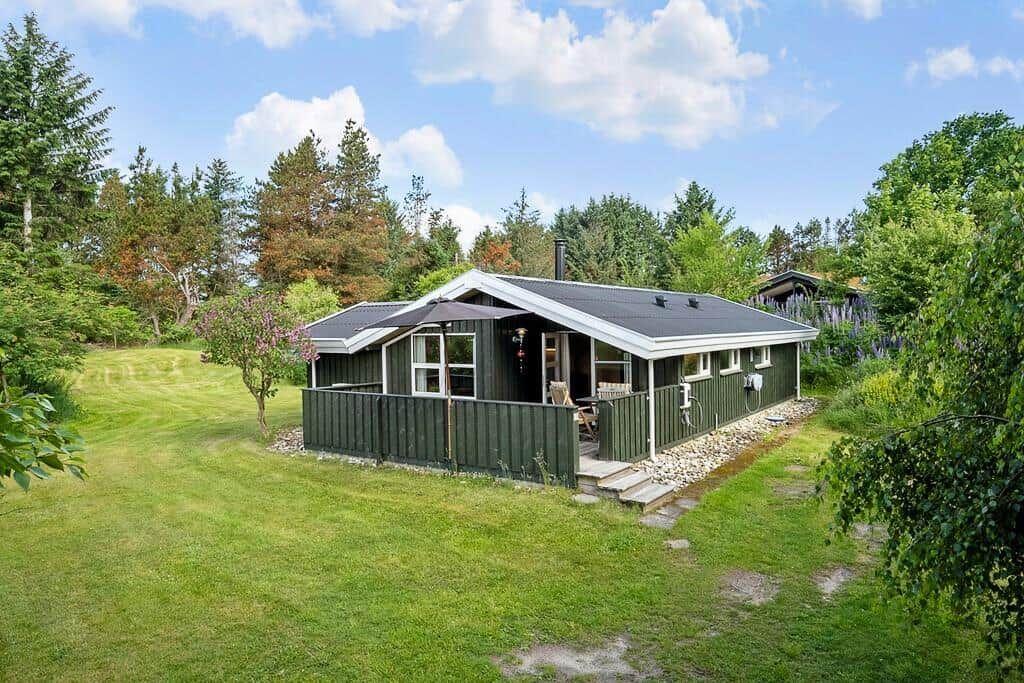 Ein grünes Ferienhaus mit Terrasse und Garten. Umgeben von Bäumen und Gras.