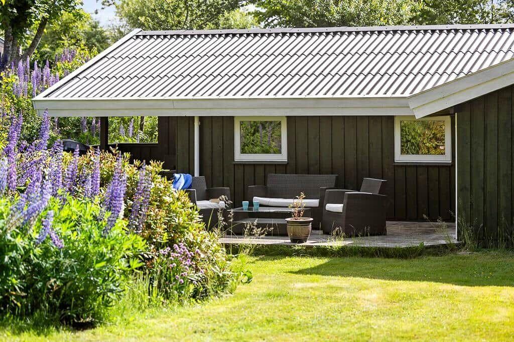 Terrasse mit Sitzgruppe unter Dach, umgeben von blühenden Lupinen und grünem Rasen.