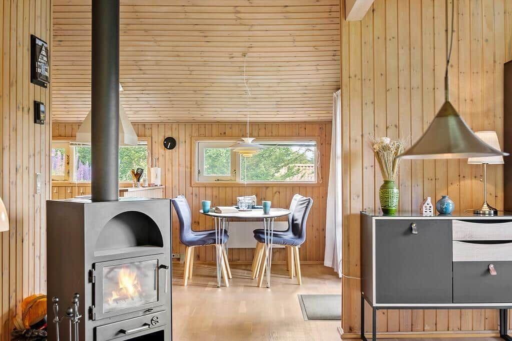 Wohnraum mit Holzwand, Esstisch, Kaminofen und Sideboard.