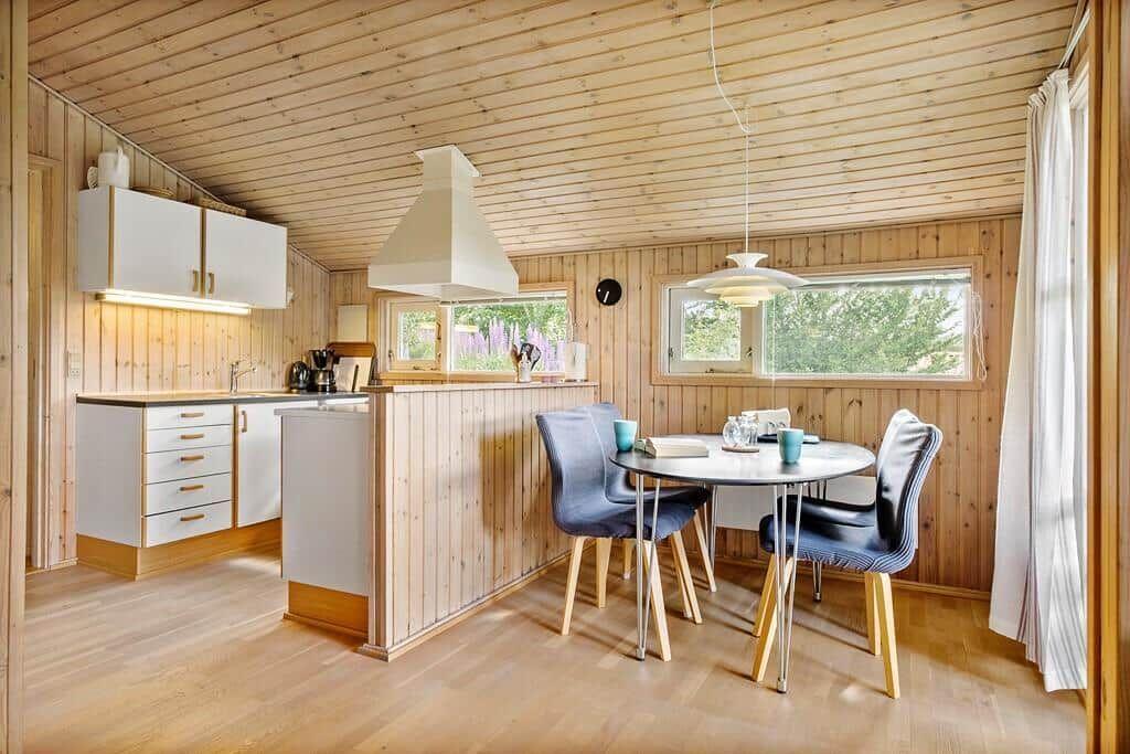 Küche mit Essbereich, Holzwand und -decke, runder Tisch mit blauen Stühlen.