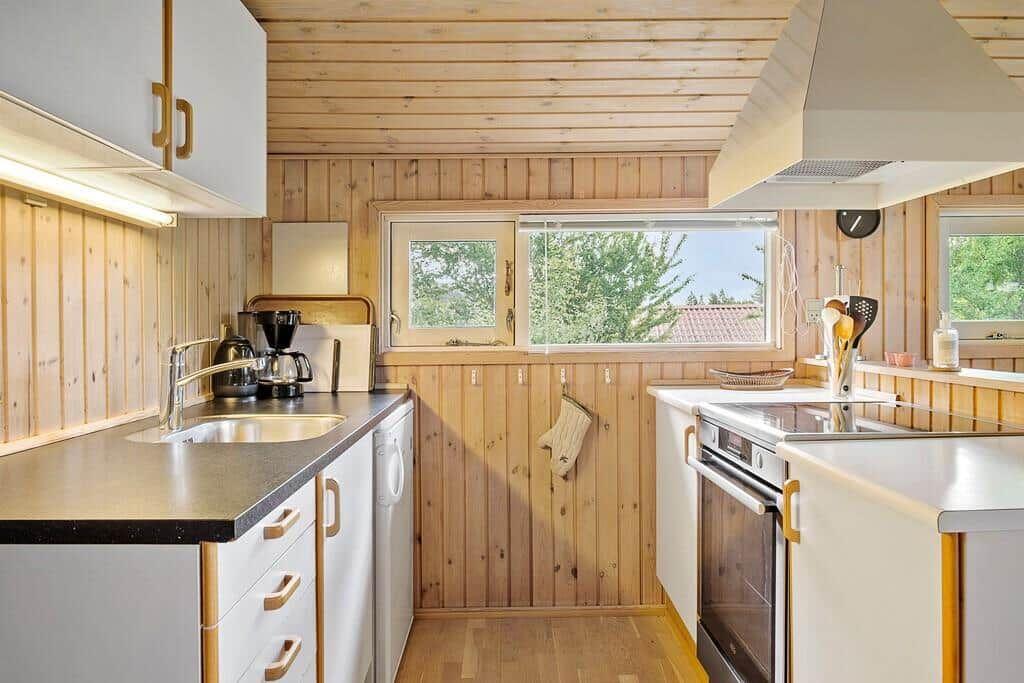 Küche mit Holzwand, Arbeitsplatte, Spüle, Herd und Fenster.