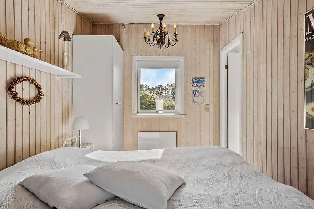 Schlafzimmer mit Holzwand, Bett, Fenster und Kronleuchter.
