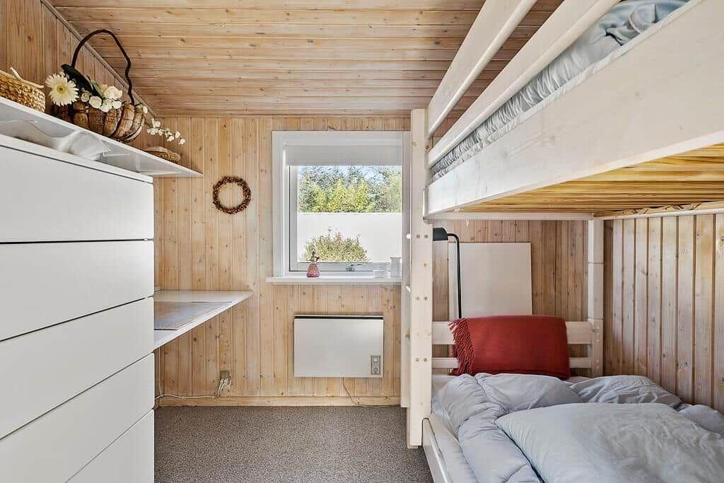 Schlafzimmer mit Hochbett, Fenster und weißen Schränken an Holzwand.