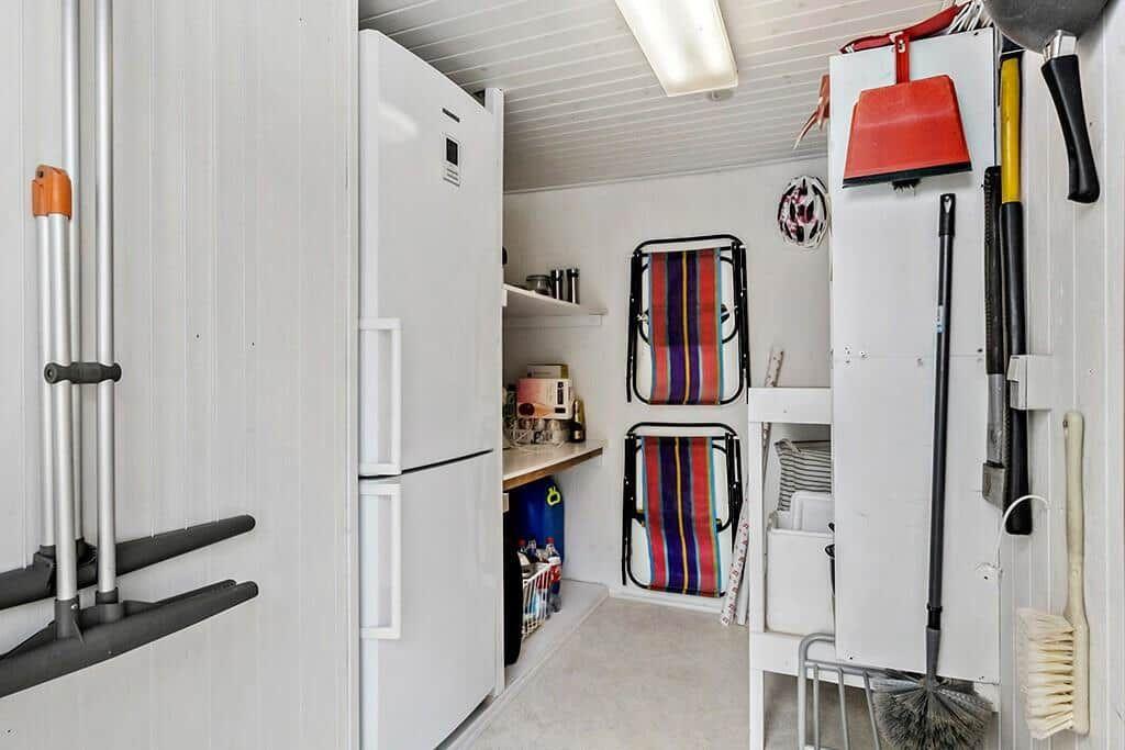Küche mit Kühlschrank, Arbeitsfläche und aufgehängten Reinigungswerkzeugen.