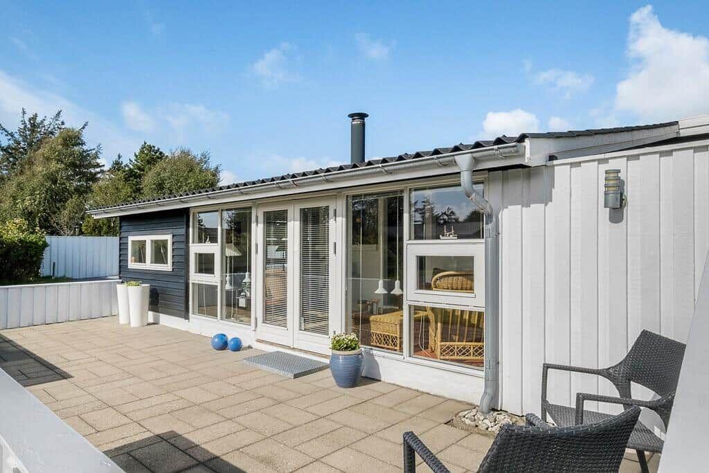Terrasse mit Sitzgelegenheiten und Blick in das Haus. Weiße Fassade und große Fenster.