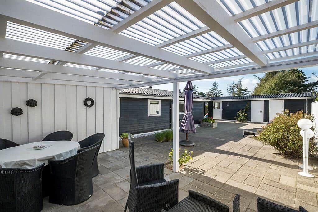 Terrasse mit Sitzgruppe unter Pavillon. Hintergrund: gepflasterter Hof mit Garten und Häusern.