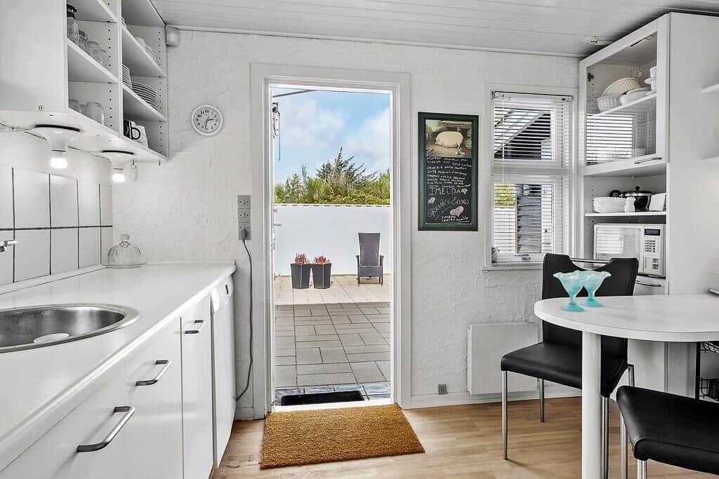 Küche mit Essbereich, Balkon und Fenster. Weiße Schränke und Holzboden.