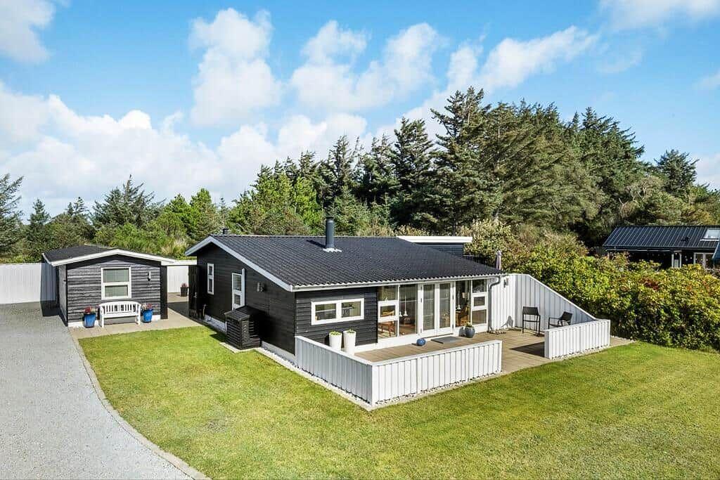 Moderne Holzhütte mit Terrasse, Garten und Wald im Hintergrund.