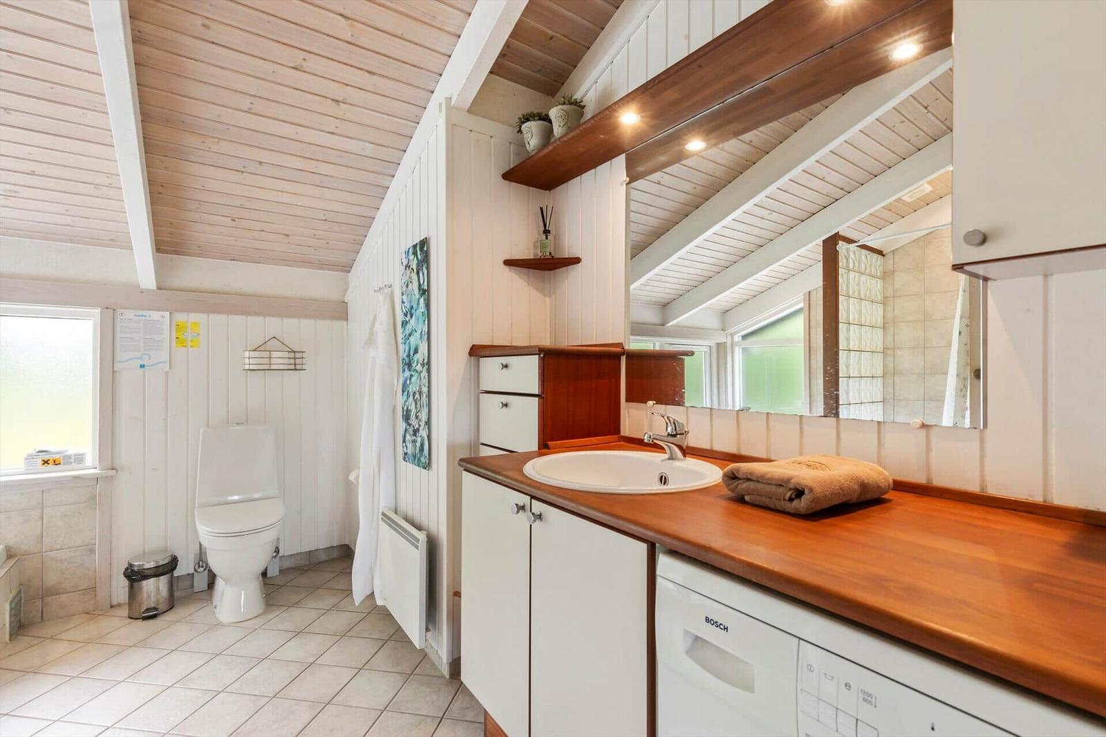Bathroom with sink, mirror, toilet, and shower. Wood countertop and white walls.