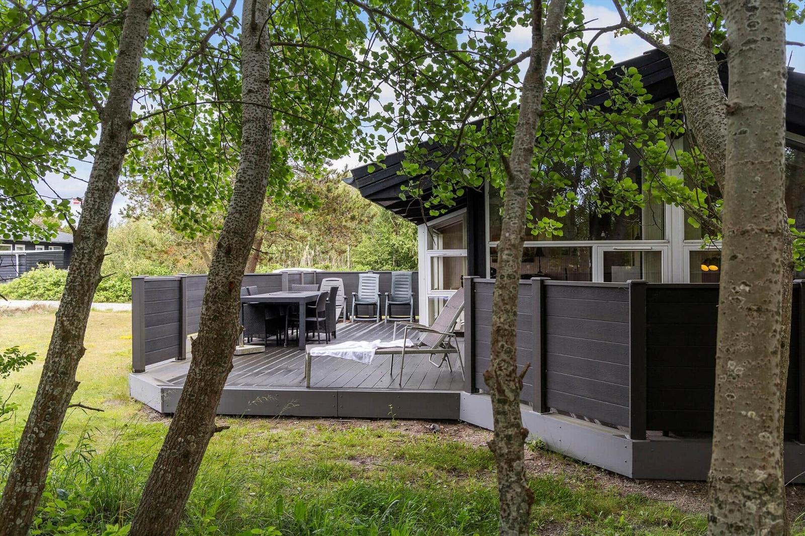 Deck with table and chairs surrounded by trees and grass.