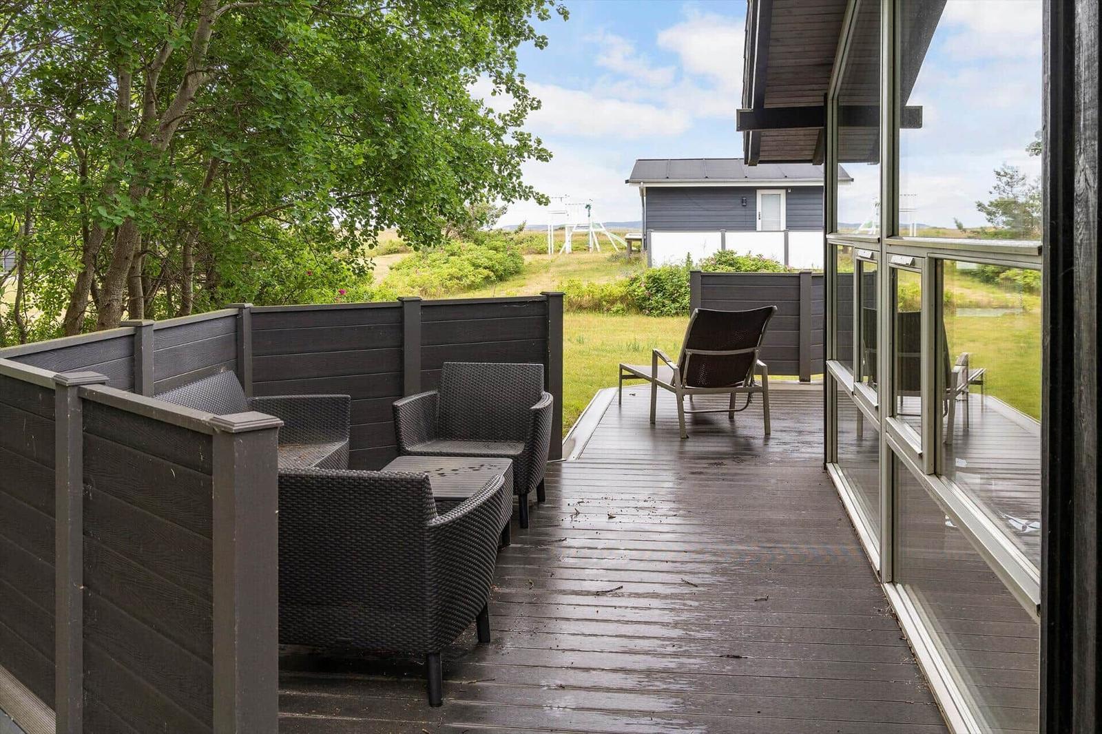 Deck with seating area and view of grassland and adjacent building.