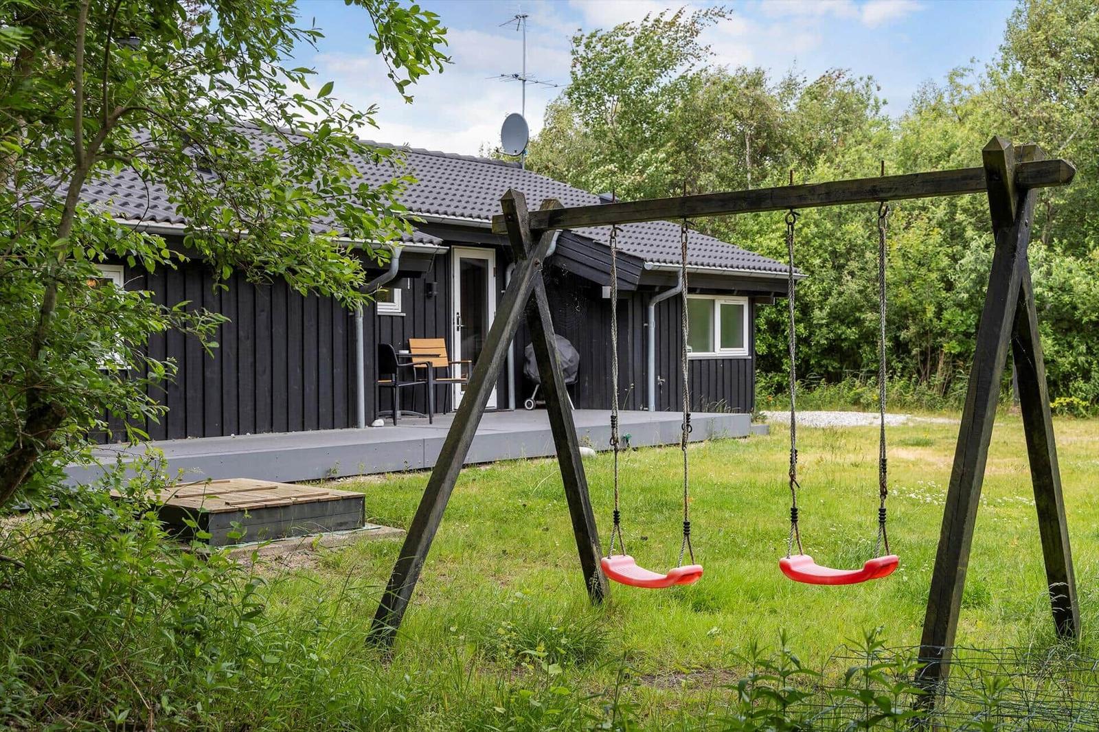 Black cabin with terrace and swing set in the garden