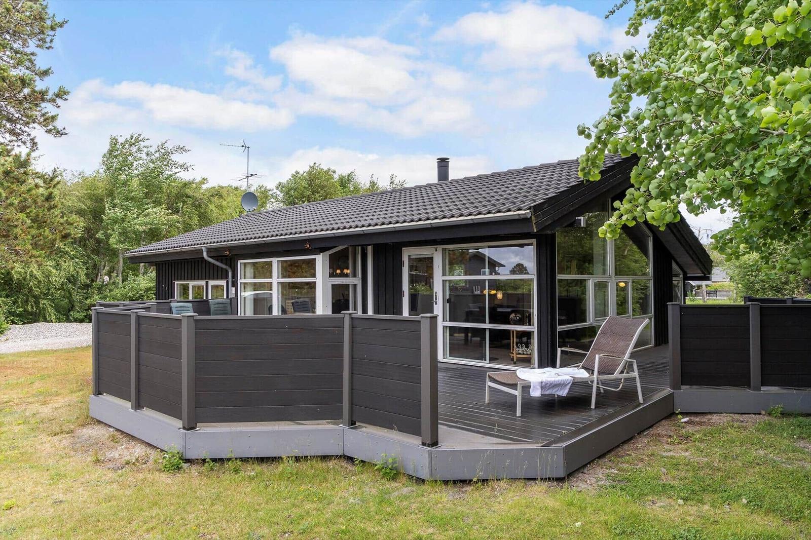 Modern villa with large balcony and glass facade. Surrounded by trees and grass.