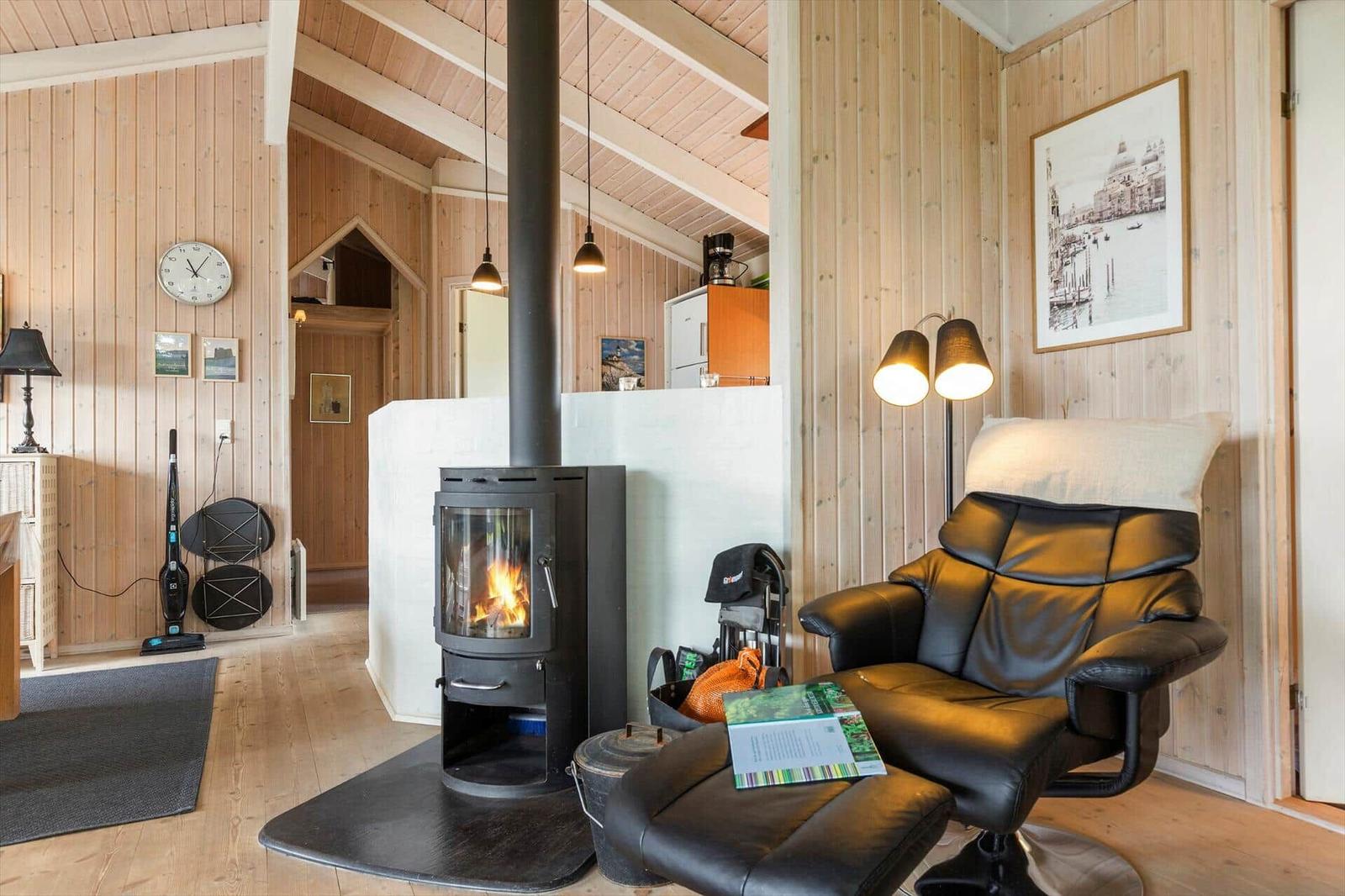 A room with wooden walls, wood stove, and black leather recliner. Wall clock and picture on the wall.