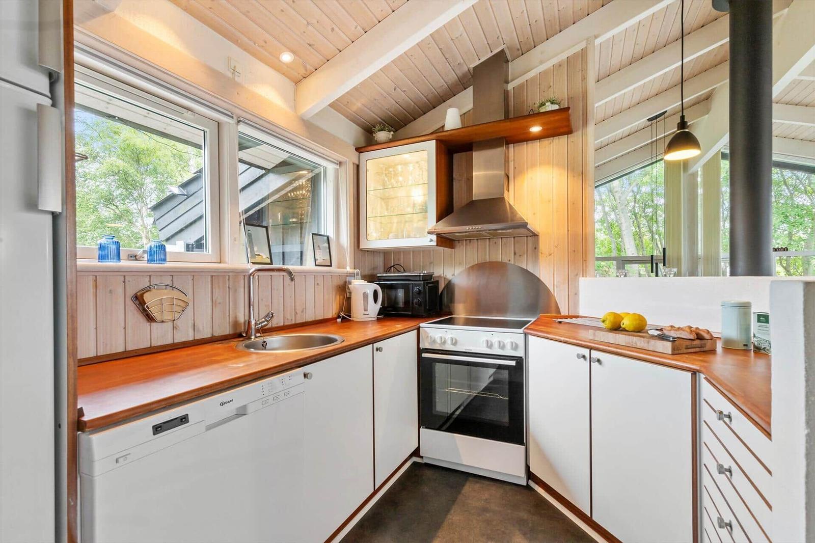 Kitchen with wooden surfaces, white cabinets, and windows overlooking trees.