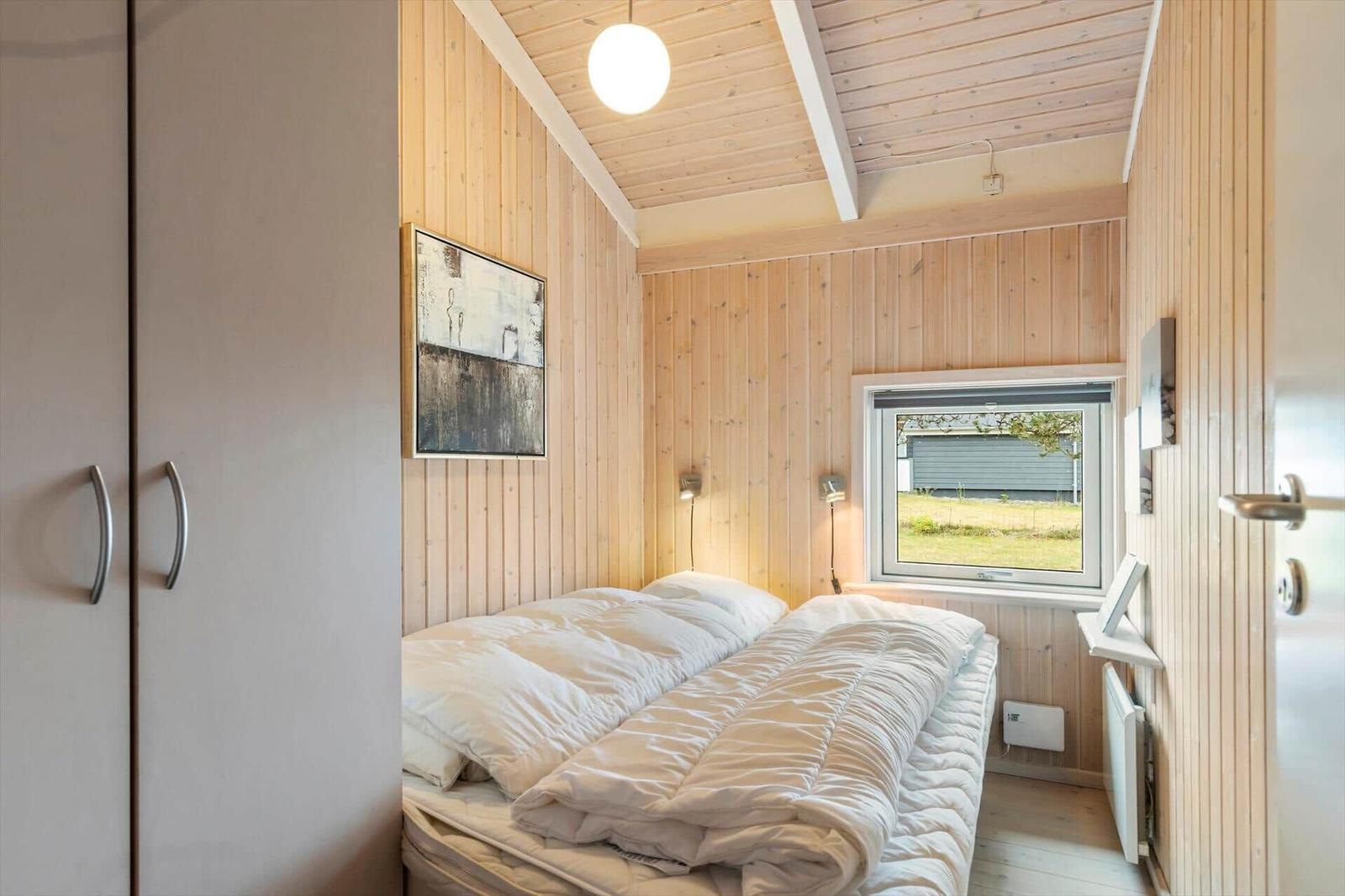 Bedroom with wooden walls, bed, and window. Small closet and wall art.