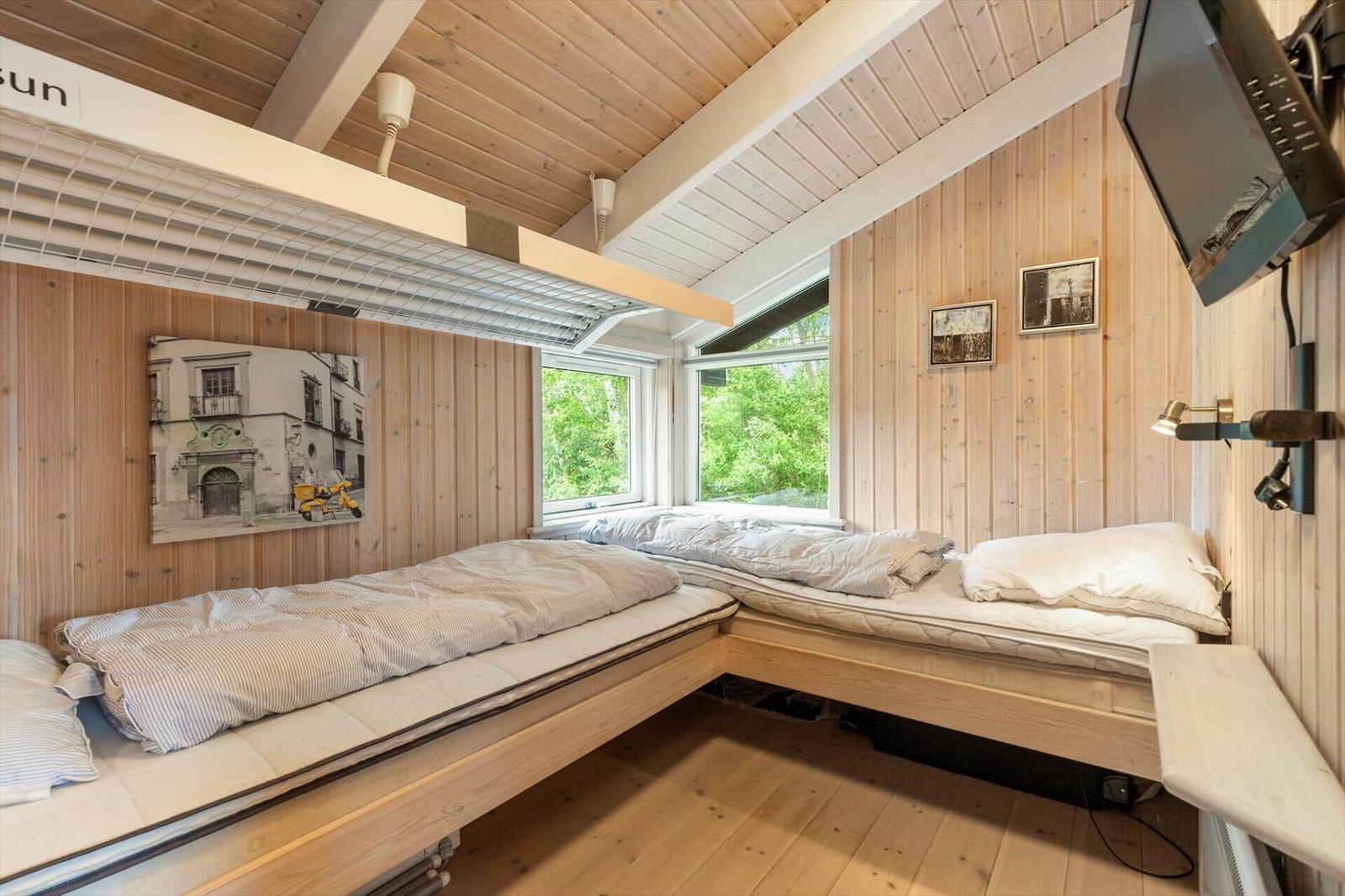Two sleeping areas with mattresses and bedding against wooden walls and ceiling. Windows with view of greenery.