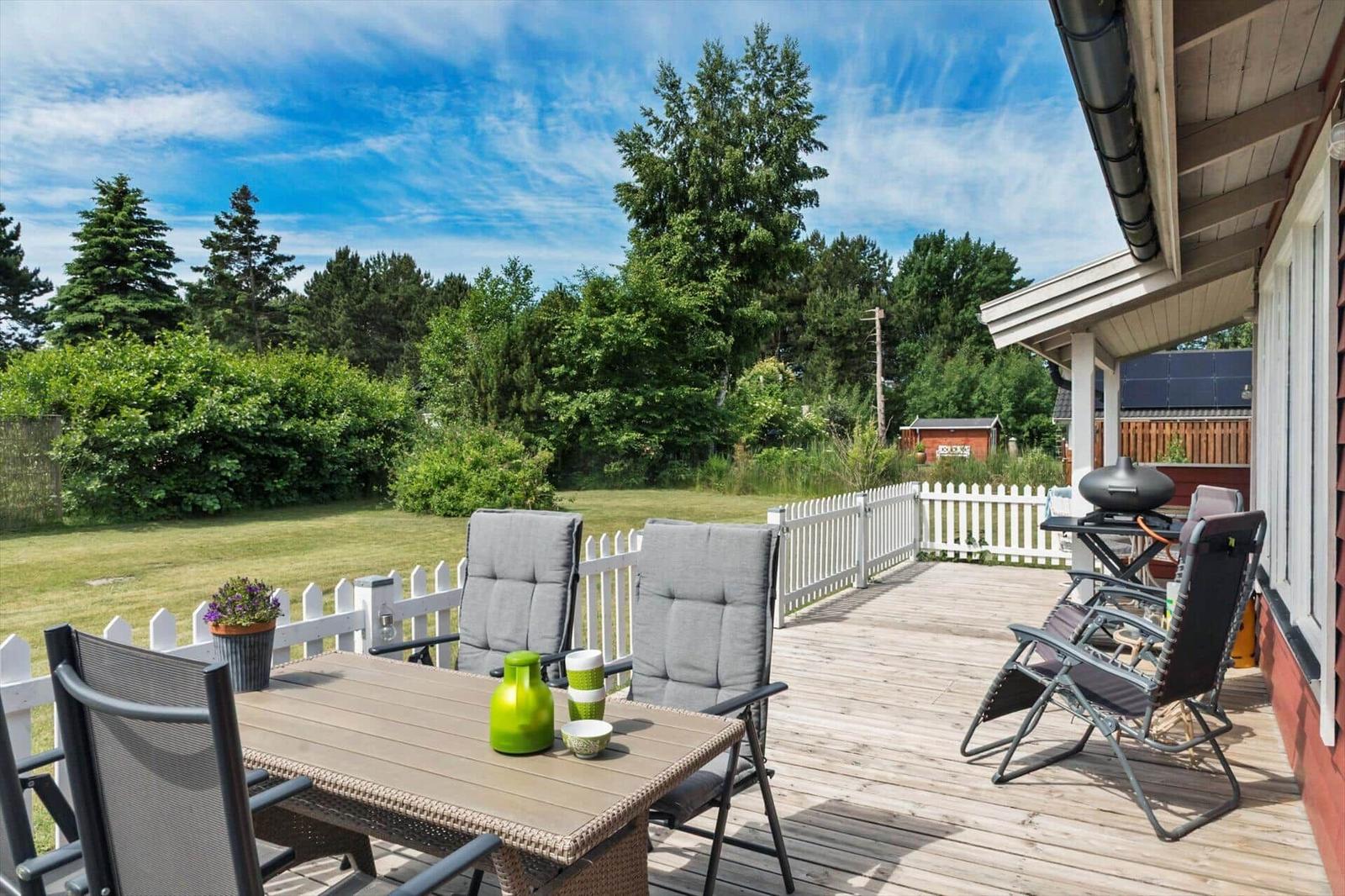 Terrasse mit Tisch, Stühlen und Grill. Grünflächen und Bäume im Hintergrund.