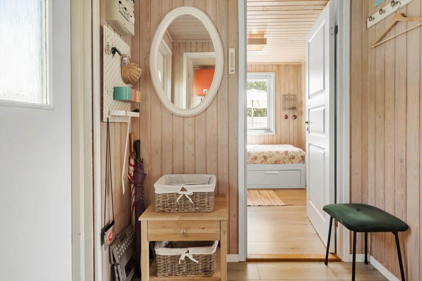 Eingangsbereich mit Spiegel, Korb und Stuhl. Durchgang zu Schlafzimmer mit Bett.