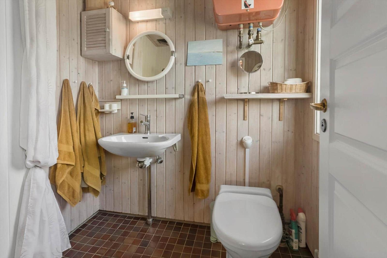 Badezimmer mit Holzwand, Waschbecken, Toilette und Handtuchhaltern.