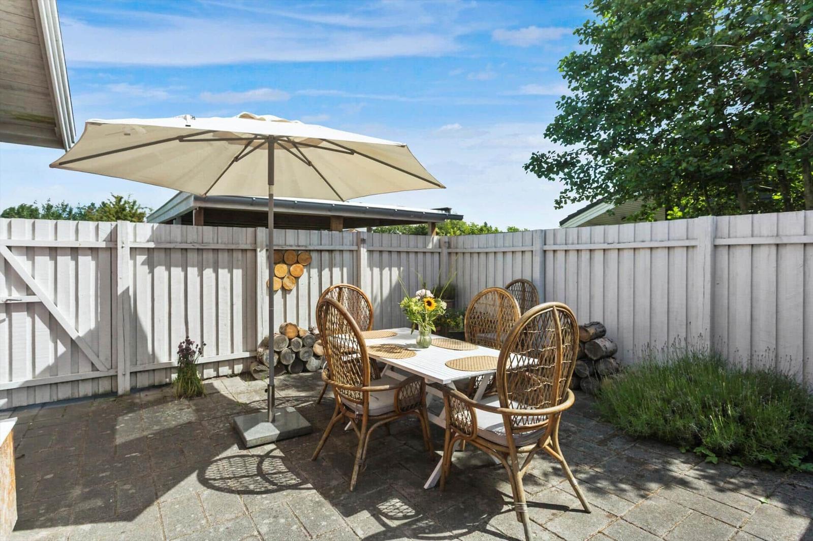 Terrasse mit Tisch, Stühlen und Sonnenschirm. Hinterhof mit Holzzaun und Pflanzen.